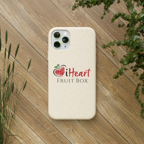 A white iHeartFruitBox Biodegradable Phone Case with tropical fruit design on a wood surface, made by Printify.