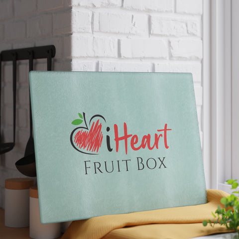 A table with a sign promoting "iHeartFruitBox Glass Cutting Board" - a selection of organically grown tropical fruits by Printify.