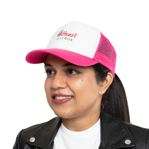 A woman wearing a pink and white hat holds a box of Printify's iHeartFruitBox Branded Mesh Cap.