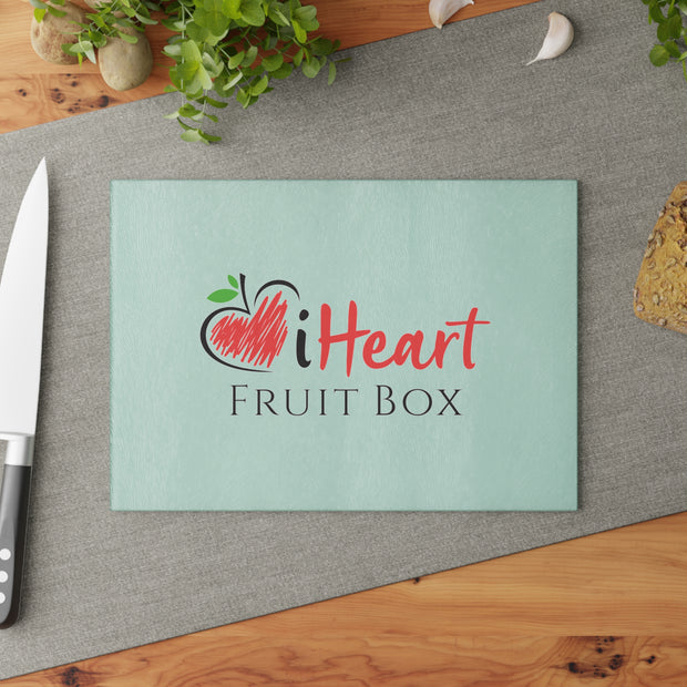 A cutting board with a knife and a cookie on a table. This setup features a Printify iHeartFruitBox Glass Cutting Board, showcasing delicious Tropical Fruit that is Organically Grown.