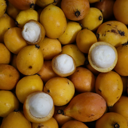 Close-up view of yellow Achachairú (Achacha) from iHeartFruitBox, some whole and some halved showing white flesh, densely packed together as an exotic tropical fruit.