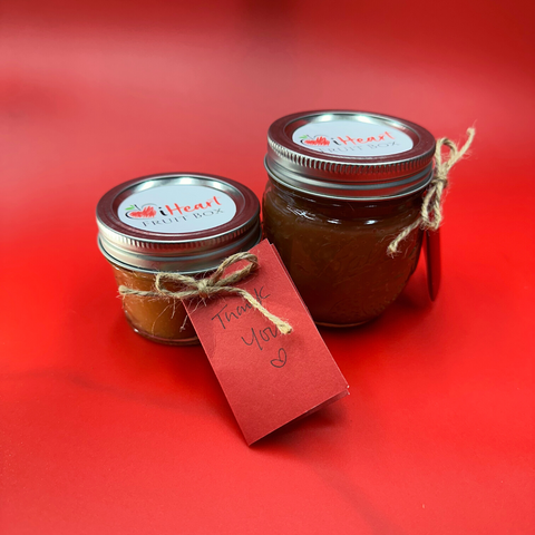 Two jars of Hidden Rose Apple jam from iHeartFruitBox on a red background.