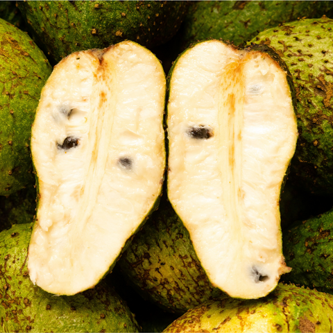 Close-up of a sliced Soursop from iHeartFruitBox showing its white, creamy interior and black seeds, with whole Soursops in the background, highlighting this tropical superfruit.